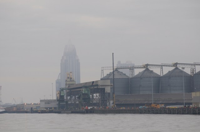 The Mobile skyline appears ghostly through the fog behind the commercial waterfront.