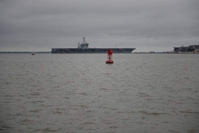 An aircraft carrier glides smoothly into port.